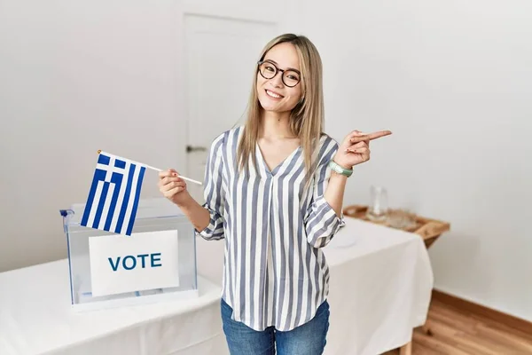 Asian young woman at political campaign election holding greece flag smiling happy pointing with hand and finger to the side