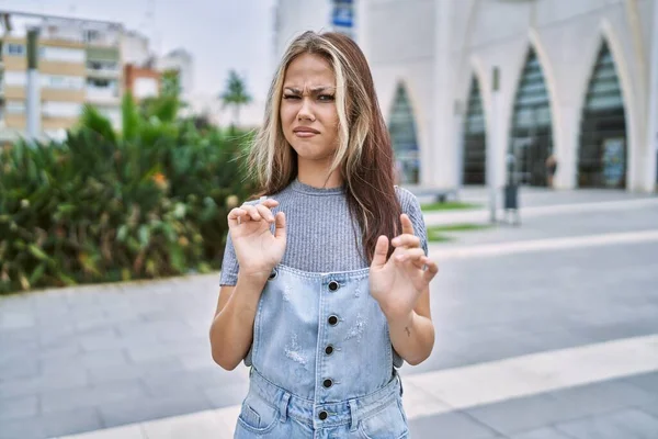 Young caucasian woman outdoors disgusted expression, displeased and fearful doing disgust face because aversion reaction. with hands raised