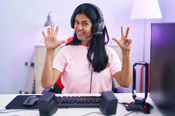 Mature hispanic woman playing video games at home showing and pointing up with fingers number eight while smiling confident and happy.