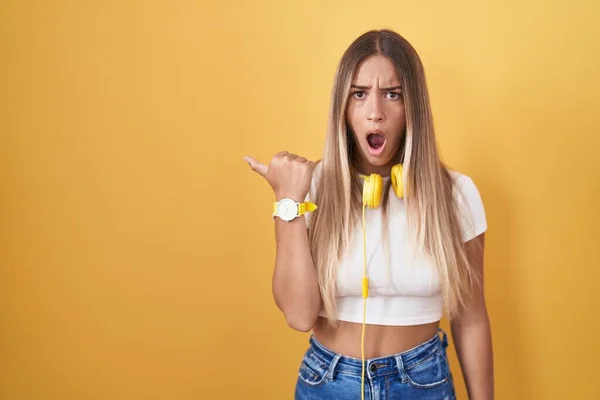 Young Blonde Woman Standing Yellow Background Wearing Headphones Surprised Pointing — Stock Photo, Image