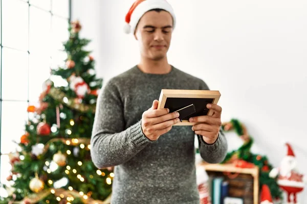 Young Hispanic Man Looking Photo Standing Christmas Tree Home — Stock Photo, Image