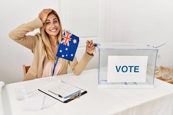 Blonde beautiful young woman at political campaign holding australian flag stressed and frustrated with hand on head, surprised and angry face