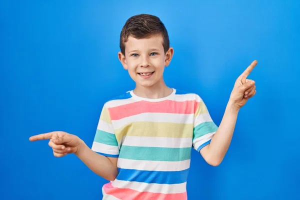青い背景の上に立つ若い白人の子供は さまざまな方向に指で自信を持って指して笑っています 広告のコピースペース — ストック写真