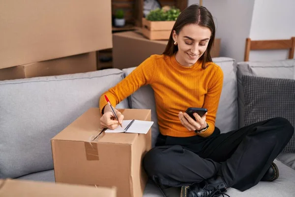 Young Caucasian Woman Using Smartphone Writing Notebook New Home — Stock Photo, Image