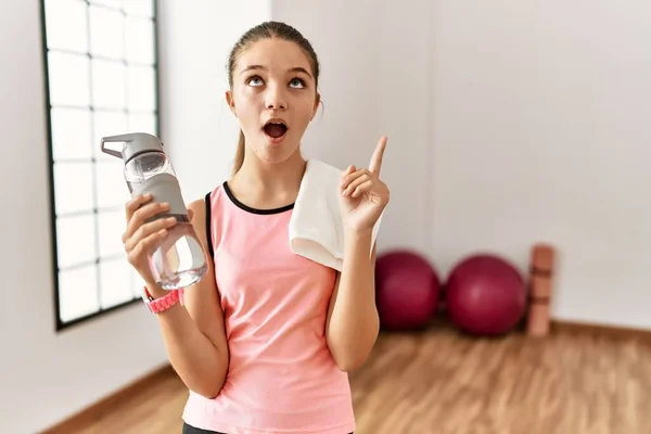 Joven Adolescente Morena Con Ropa Deportiva Sosteniendo Botella Agua Asombrada —  Fotos de Stock