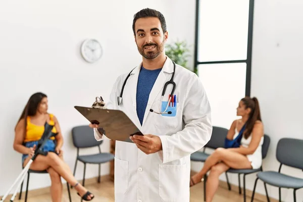 Young Hispanic Doctor Smiling Happy Holding Clipboard Standing Medical Clinic — стоковое фото