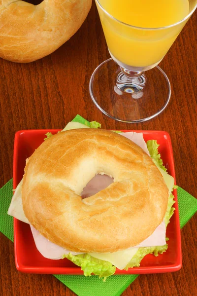 Bagel with ham, cheese and lettuce and orange juice — Stock Photo, Image