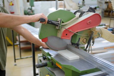 Mobilya fabrikasında çalışan bir işçi dairesel testere ile beyaz bir odun kesiyor.