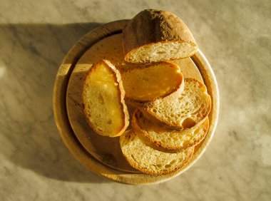Dilimlenmiş somun ekmek, yuvarlak ahşap bir kesme tahtasının üzerinde, otlayan sabah ışığı, üst manzara