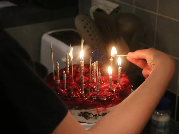 La mano enciende velas en un pastel rojo — Foto de Stock