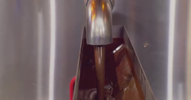 Moderne apparatuur voor industriële voedselproductie.hete gesmolten chocolade wordt gegoten uit een metalen container door middel van een tap.close-up — Stockvideo