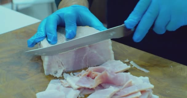 Manos en guantes jamón cortado con un cuchillo en una tabla de corte.close-up — Vídeos de Stock