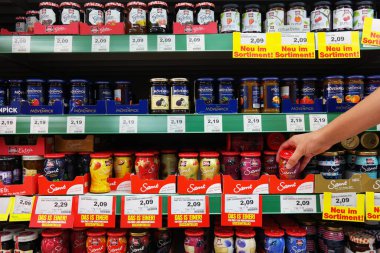 GERMANY - AUGUST 2016: Shopper selecting preserves of shelves filled with different brands of marmalade jars in a Marktkauf Hypermarket.