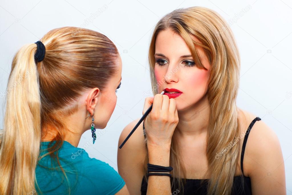 Makeup artist applying lipstick on model's lips Stock Photo by