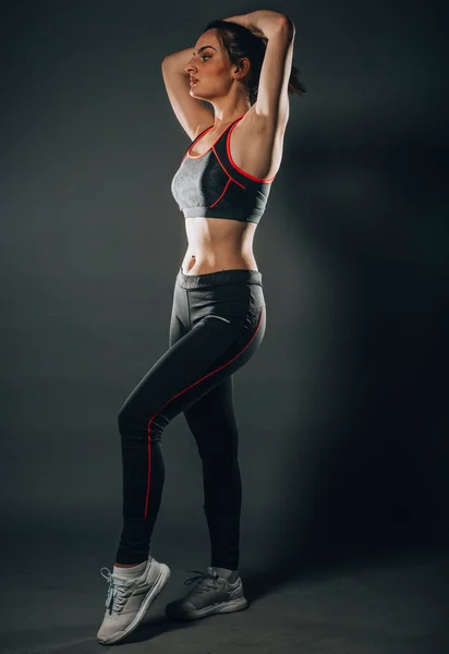 Sportive strong woman in black sportswear makes fitness training - forward lunge, isolated at dark studio