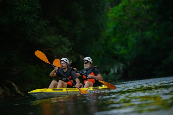 年轻的成年人和年长的皮划艇手正在森林河里一起划船 — 图库照片
