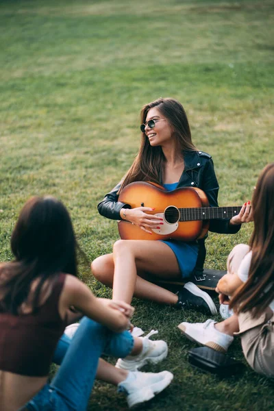 魅力的な女の子はギターを演奏しており 彼女の友人と一緒に楽しんでいます — ストック写真