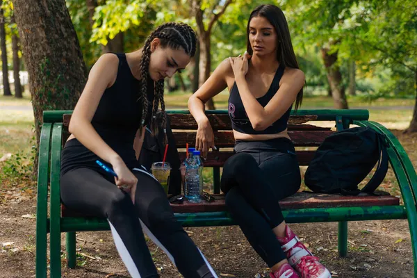 Дві Дівчини Сидять Парку Відпочиваючи Від Роликових Ковзанів Які Ють — стокове фото