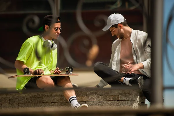 两个男性朋友正坐在墙上谈论溜冰鞋 — 图库照片
