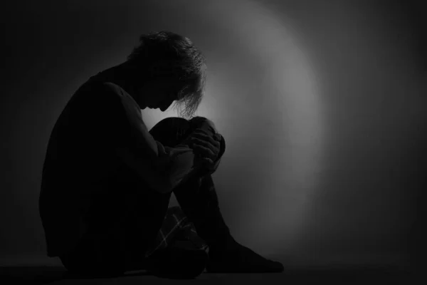 忧郁而悲伤的男孩坐在那里抱着他的腿哭泣的轮廓 — 图库照片