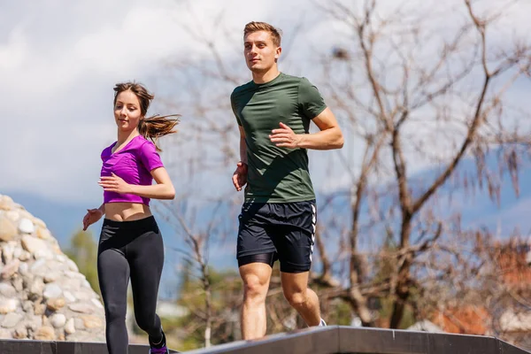 スポーツカップルは公園で一緒に走る フィットネストレーニングの屋外で一緒にジョギングする若者 一緒にスポーツトレーニングで男と女 — ストック写真