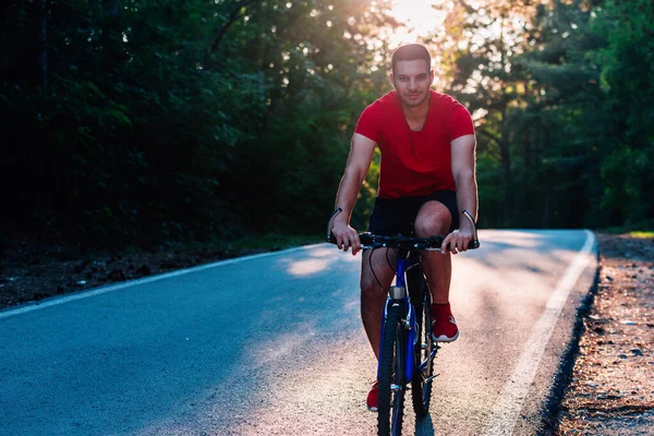 骑自行车的男骑手在日落时分骑自行车在穿越深林的路上 极限运动者无安全设备 — 图库照片
