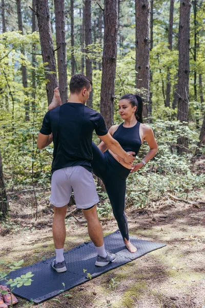 若いアクティブなカップルは ジョギングやランニング後にヨガマットで森の中でストレッチ演習を行う — ストック写真