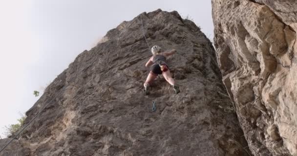 トップに到達するための戦略を考えながら魅力的な女の子は大きな岩を登っています — ストック動画