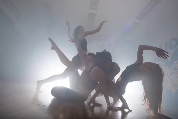 煙と照明で暗いスタジオでファンキーなヒップホップの動きを楽しんでいる多人種のダンサーのグループ 舞台上で活躍する若手ヒップホップダンサーのグループ 幸せな踊りの女性 — ストック写真
