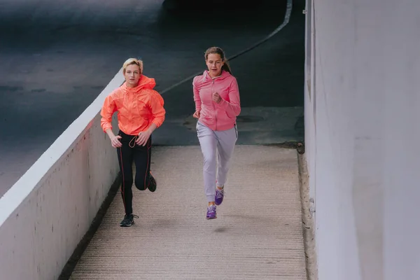 迷人的女运动员白天在城市灰墙建筑中奔跑 — 图库照片