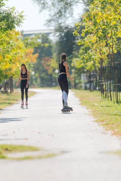 公園内の都市の通りに屋外に乗るローラースケートの2人の若いフィット女性のレビュー — ストック写真