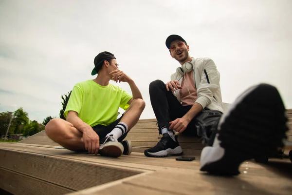 Due Amici Vestiti Casual Sorridono Siedono Sulla Panchina Mentre Parlano — Foto Stock