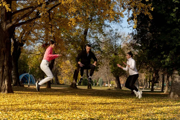 3人の魅力的で素晴らしい友人が公園でのトレーニングの前に暖かくなるためにジャンプしています — ストック写真