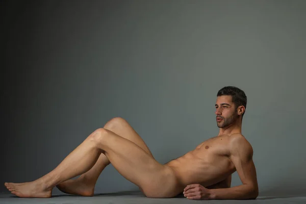 Fashion nude photo of a male model with seductive figure lying isolated on the floor in a studio