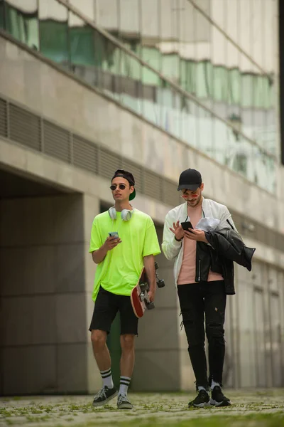 Two guy friends are walking and talking together while checking theie phones