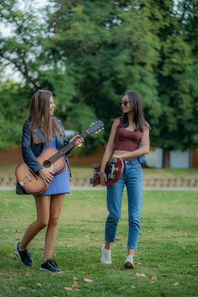 二人の魅力的で美しい女の子は笑顔で 彼らのギターとスケートを保持しながら話しています — ストック写真