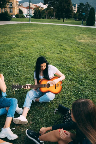 黑发美女正在公园为她的朋友们弹奏吉他 — 图库照片