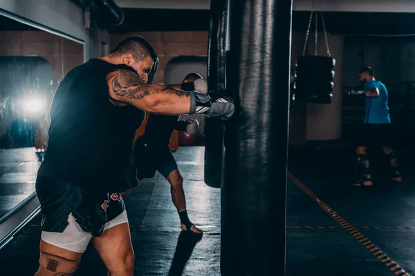 Heavy male kick boxer hitting a huge punching bag at a boxing studio. Man boxer training hard