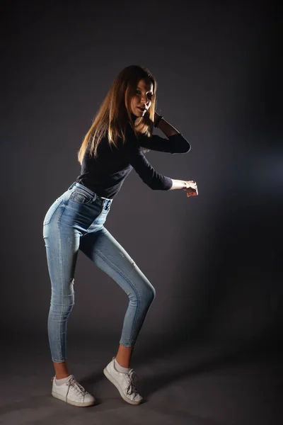 サイド全身ポートレートの若い女性モデルで黒トップとジーンズポージングで1本足で前 — ストック写真