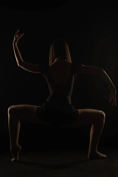 Young ballerina is holding a great squat pose in studio, silhouette
