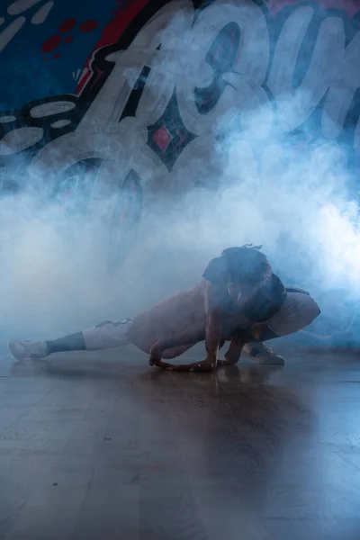 Young man break dancing in club with lights and smoke.