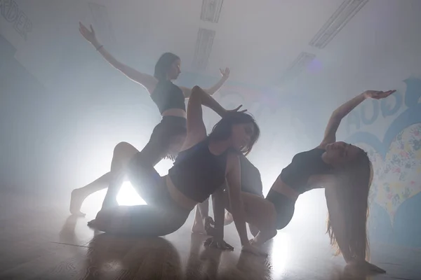 Group of multiracial dancers enjoying funky hip hop moves in dark studio with smoke and lighting. Group of young hip-hop dancers performing on the stage. Happy dancing women.