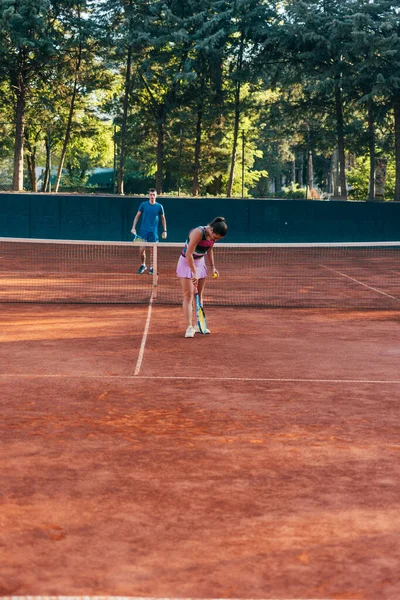 A young female tennis player serving on a clay court