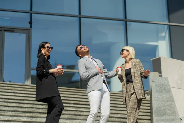 Three business people with sunglasses are laughing while drinking coffee on their break