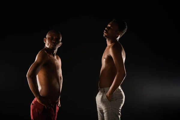 Two topless black males are posing in studio with only  their jeans on