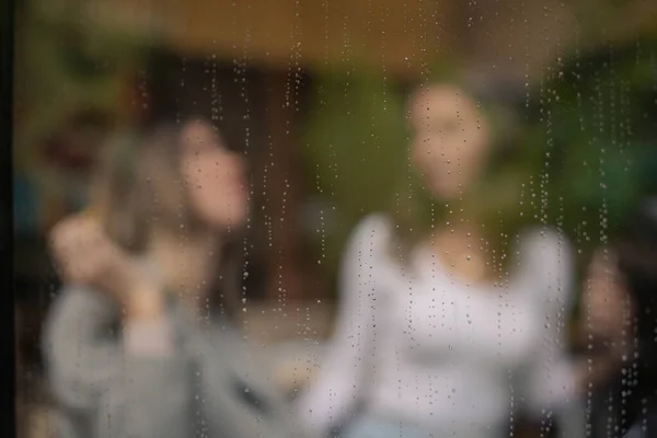 Clean window with rain drops on it, girls in blur sitting and talking in the lunch bar