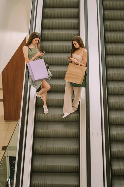 Alışveriş Merkezindeki Yürüyen Merdivende Telefonlarına Bakan Iki Güzel Kız — Stok fotoğraf