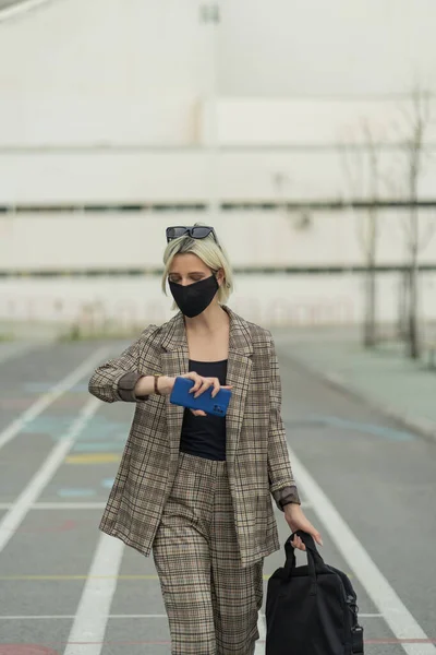 Businesswoman is walking towards the company with her mask on while chekcing the time