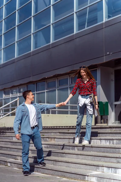 Pretty couple walking on the stairs in front of the building while holding hands and smiling