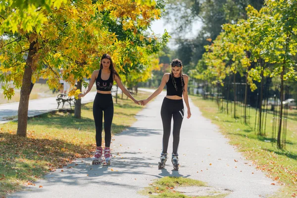 美丽的女友们 骑着溜冰鞋 手牵手在街上 — 图库照片